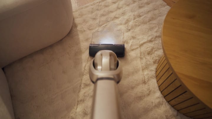 Cordless Stick Vacuum Cleaning A Soft Beige Rug In A Modern Living Room