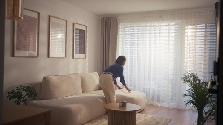 Woman Bending Over Cream Sofa In Bright Modern Living Room Morning