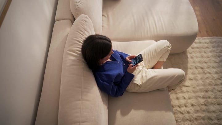 Woman Lying On Sofa Checking Smartphone In Modern Living Room