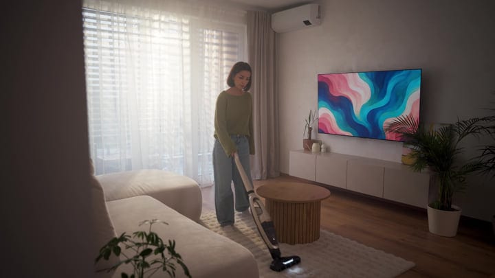 Woman Vacuuming Living Room Rug With Cordless Cleaner In Bright Sunlight