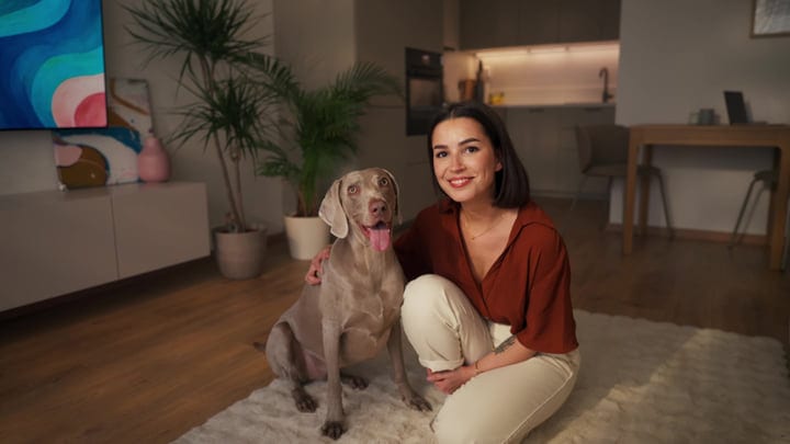 Young Woman And Weimaraner Dog Smile While Relaxing On A Living Room Rug