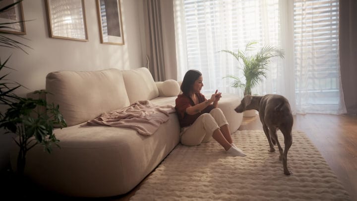 Woman Sits On Floor With Phone And Dog In Bright Living Room