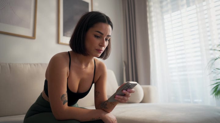 Woman Sits On Sofa Looking At Her Phone In A Bright Living Room