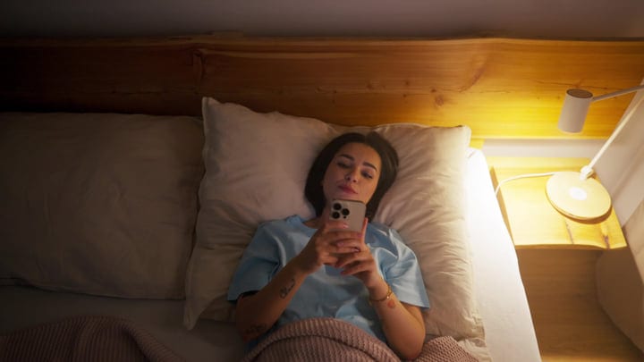Woman Relaxing In Bed With Smartphone By Soft Lamp Light