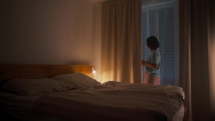 Woman Checks Her Smartphone By Bedroom Window Early Morning Light