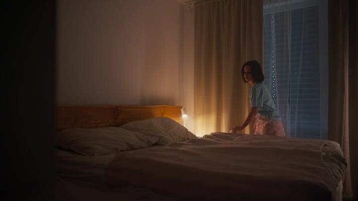 Woman Arranging Bedding In Her Warmly Lit Bedroom Early Morning