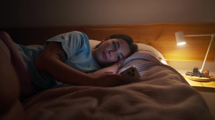 Young Woman Quietly Scrolling Her Smartphone While Lying In Bed