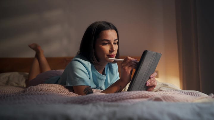 Young Woman Using A Digital Tablet And Stylus Lying On A Bed