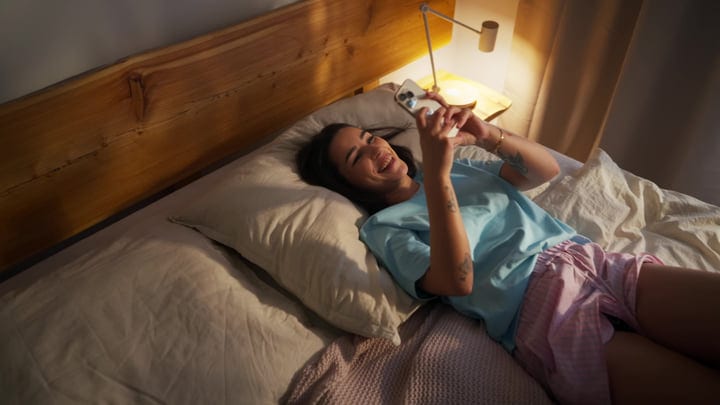 Smiling Woman Enjoying Her Morning Routine With Smartphone In Cozy Bed