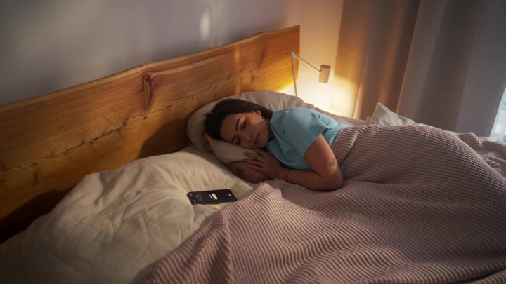 Woman Sleeping In Bed With Smartphone Alarm Next To Her
