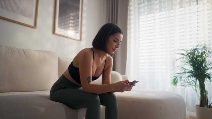 Woman Relaxing On Sofa Checking Smartphone In Bright Home