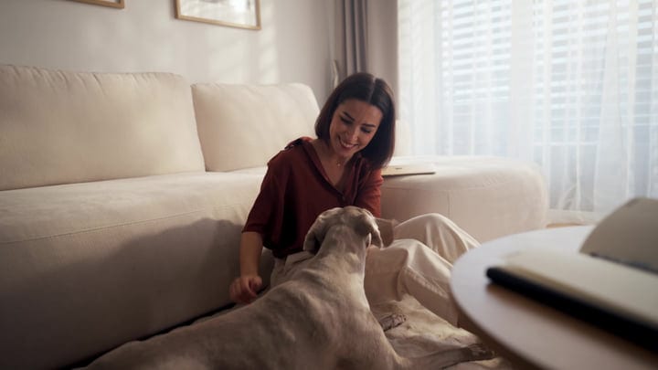 Young Woman Smiling While Petting Her Dog On Living Room Floor