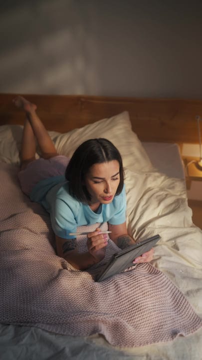 Woman Lying In Bed Using Digital Tablet With Stylus In Morning Light