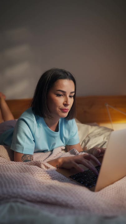 Woman Lying Comfortably On Bed And Typing On Her Laptop