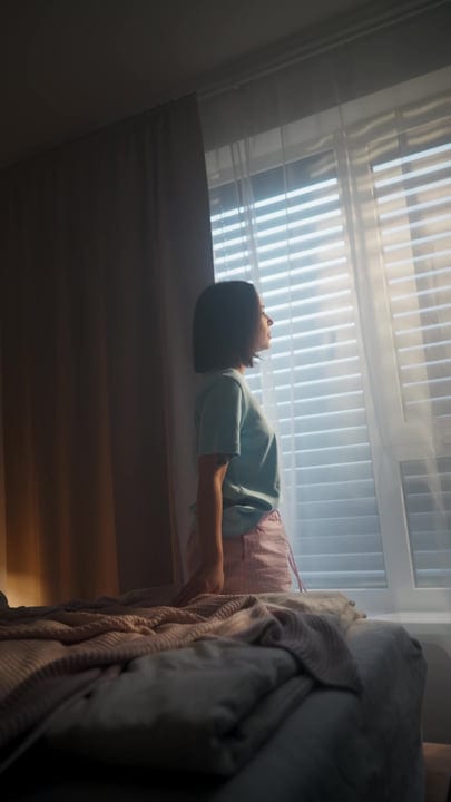Woman Standing By Bedroom Window Gazing Out Into The Morning Sun