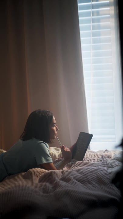 Woman Lying On Bed With Stylus And Tablet Near Window In Gentle Morning Light