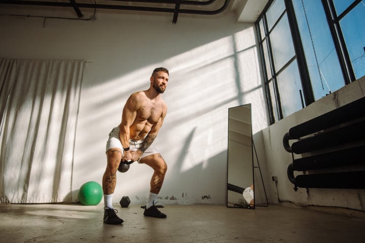 Muscular Man Performing Kettlebell Squats In A Bright Industrial Gym Studio