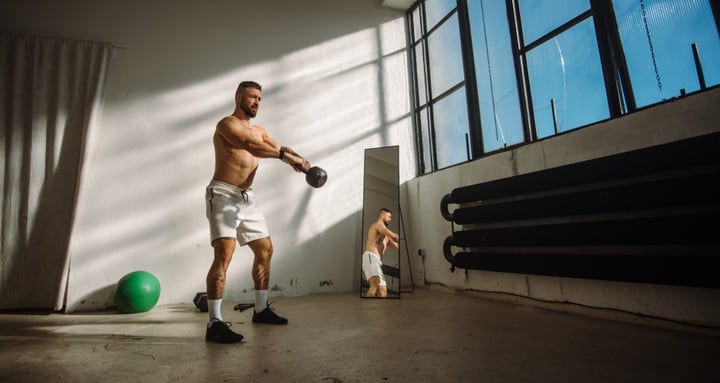 Muscular Man Performs Kettlebell Swings In A Bright Industrial Gym