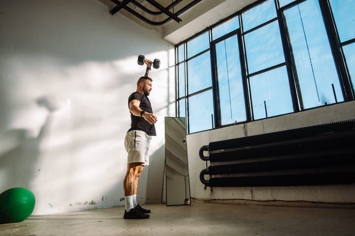 Man Performing Single Arm Overhead Dumbbell Press In Modern Industrial Gym
