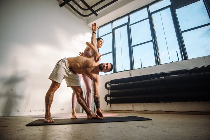 Man And Woman Practicing Assisted Triangle Yoga Pose In Bright Studio