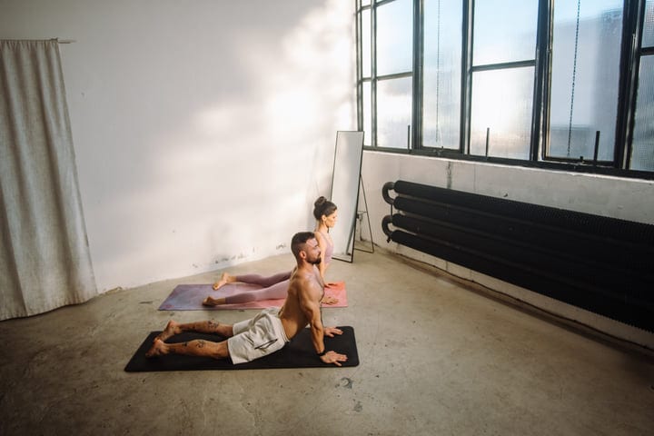 Man And Woman Practice Yoga Cobra Pose Indoors In A Bright Studio
