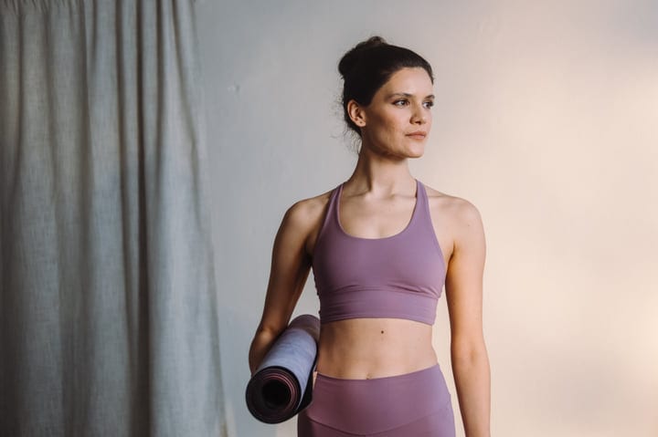 Woman Standing With Yoga Mat Indoors Looking Away