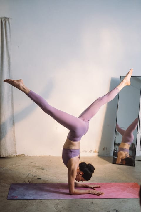 Woman Holds Forearm Stand With Split Legs On Mat In Bright Studio