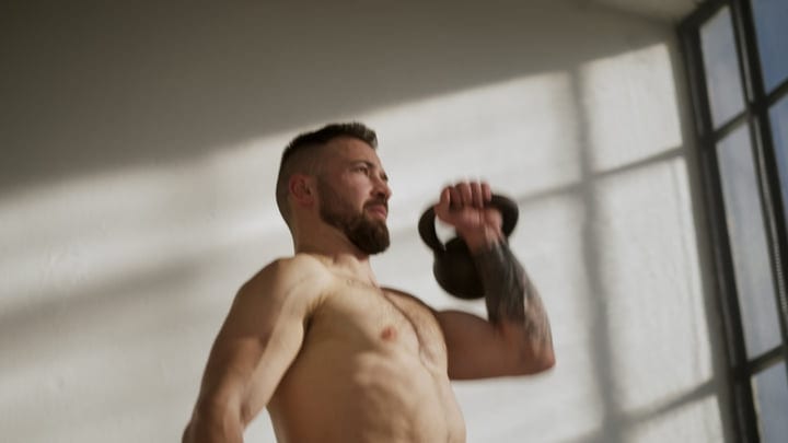 Muscular Man Exercising With Kettlebell In Bright Indoor Fitness Space