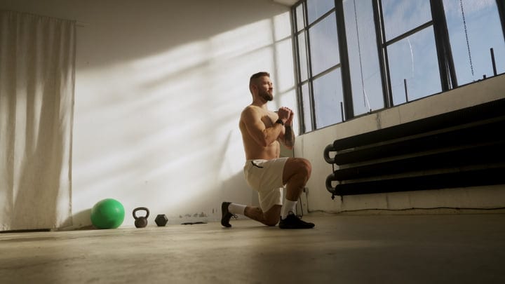 Man Performs Lunges In Bright Studio With Kettlebell And Exercise Ball