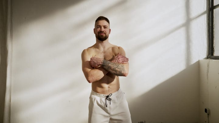 Man With Tattoos Poses Confidently Indoors With Arms Crossed