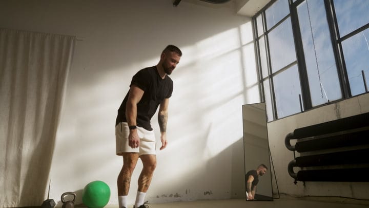 Man Bending Down With Kettlebell And Exercise Ball In Bright Gym