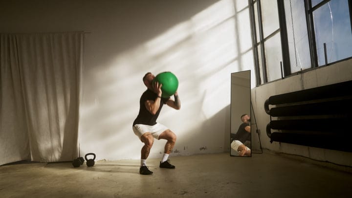 Man Performing Medicine Ball Squats In Bright Urban Fitness Studio