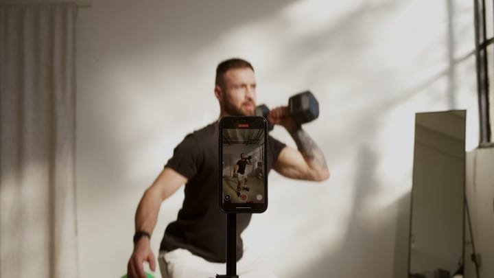 Man Records Dumbbell Workout Session With Smartphone In Modern Studio