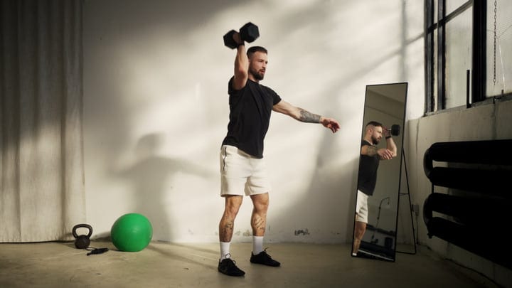 Man Lifting Dumbbell Overhead In An Indoor Gym With A Mirror