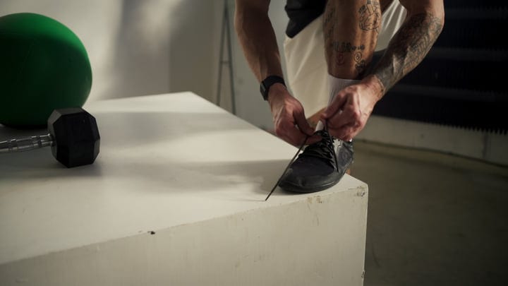 Man Tying Black Athletic Shoe Before Workout In Modern Indoor Gym