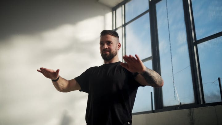 Man Practices Yoga Pose Indoors Near Window With Sunlight