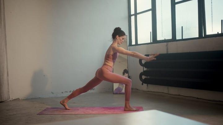 Young Woman Practices Yoga Lunge Pose On Pink Mat In Bright Studio