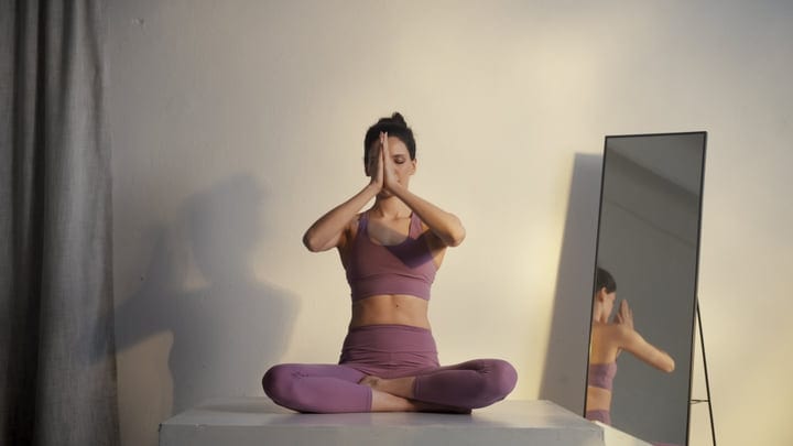 Young Woman Meditating in Lotus Position Indoors with Hands in Anjali Mudra