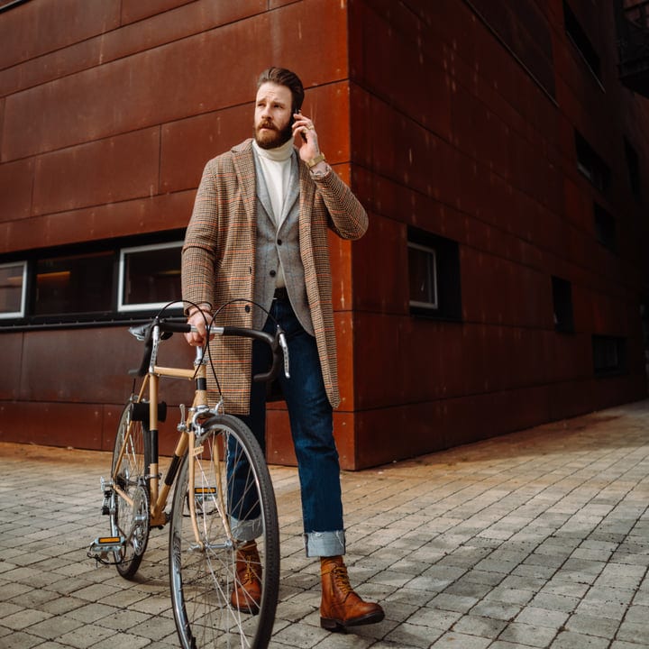 Bearded Businessman Talking On Smartphone While Holding Bicycle On Urban Street