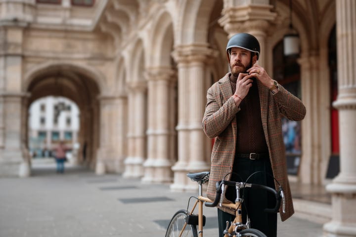 Bearded Man Adjusting Bicycle Helmet Strap In Front Of European City Building