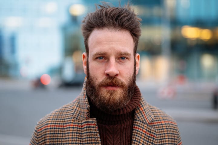 Bearded man in a tweed coat standing in an urban area during his commute