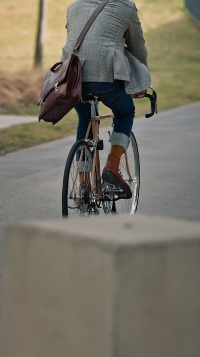 Businessman Cycling Through Urban Park With Leather Bag